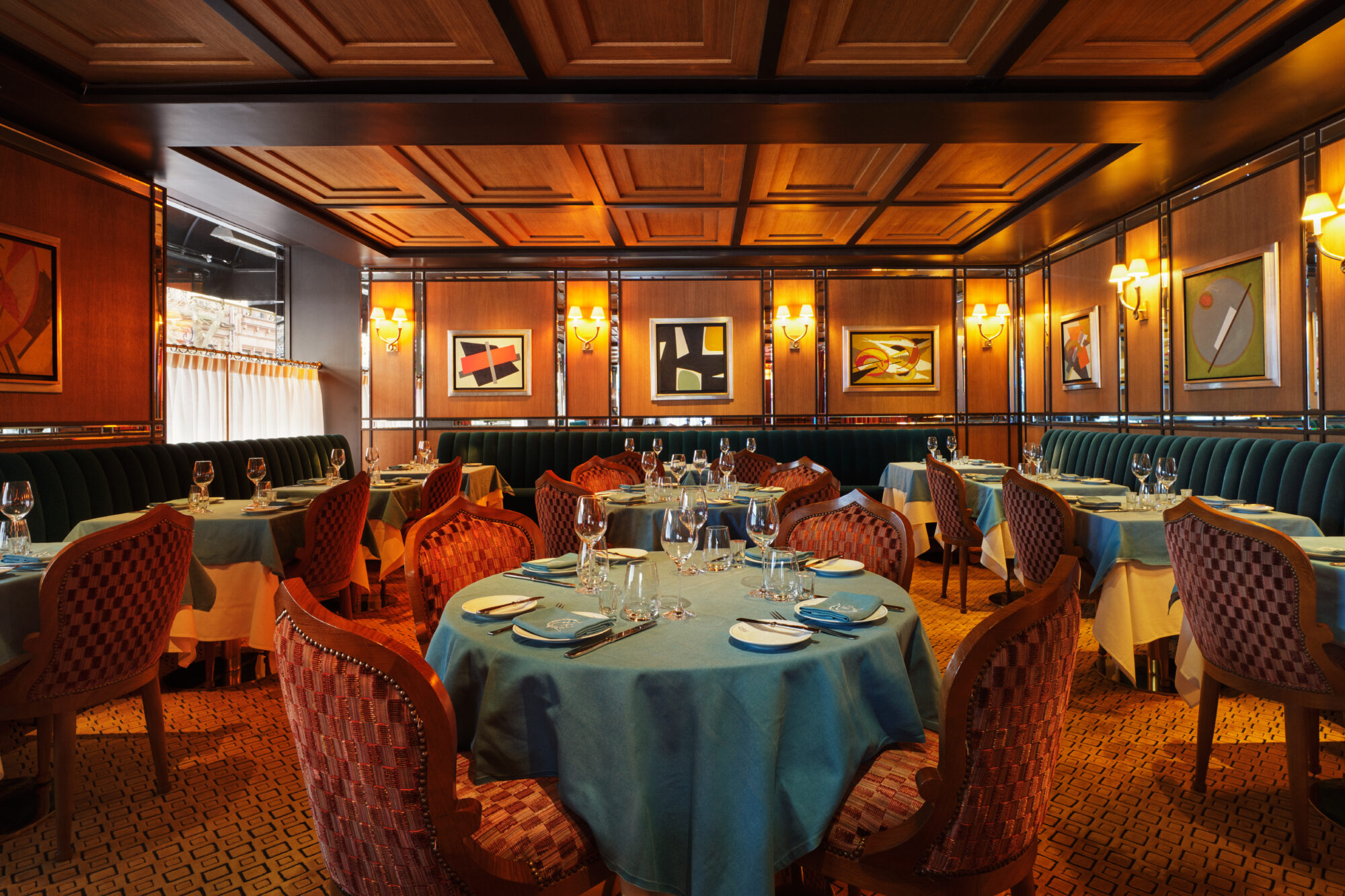 A dining room with round tables set for meals, red chairs, and artwork on the walls.