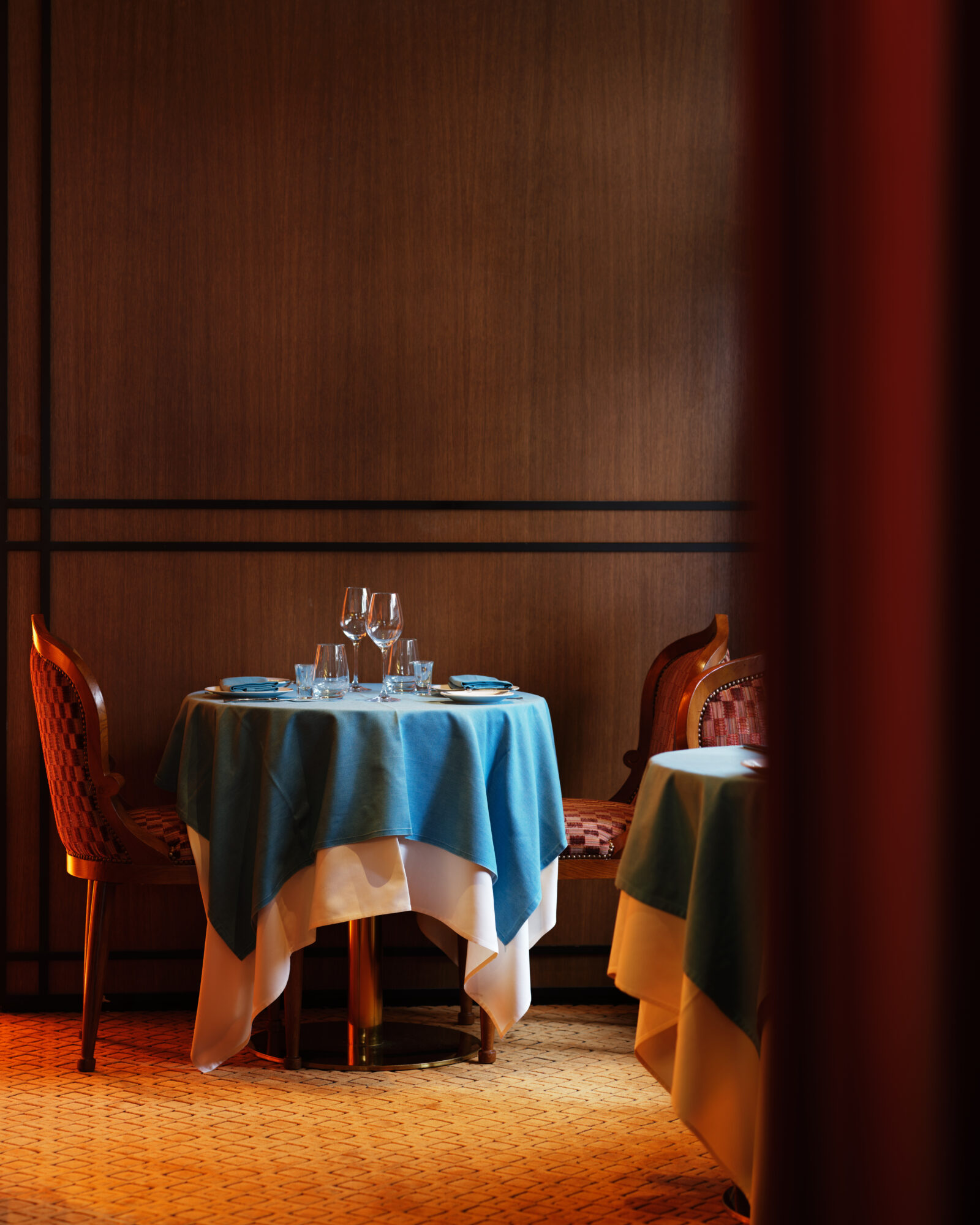 A dining area with a table set for two, wooden chairs, and wood paneling on the walls.