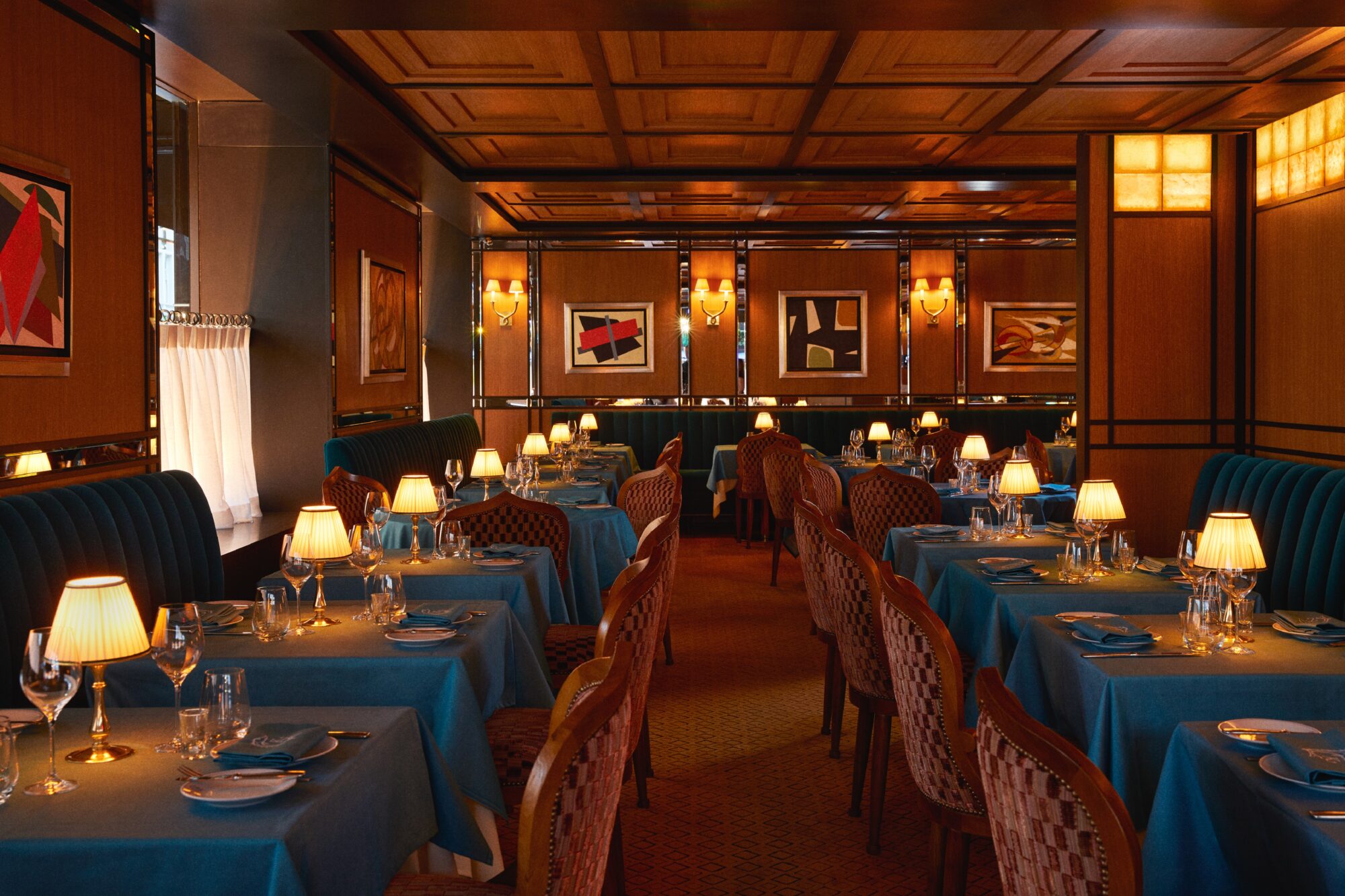 A formal dining room with blue tablecloths, lamps, and artwork on the walls.