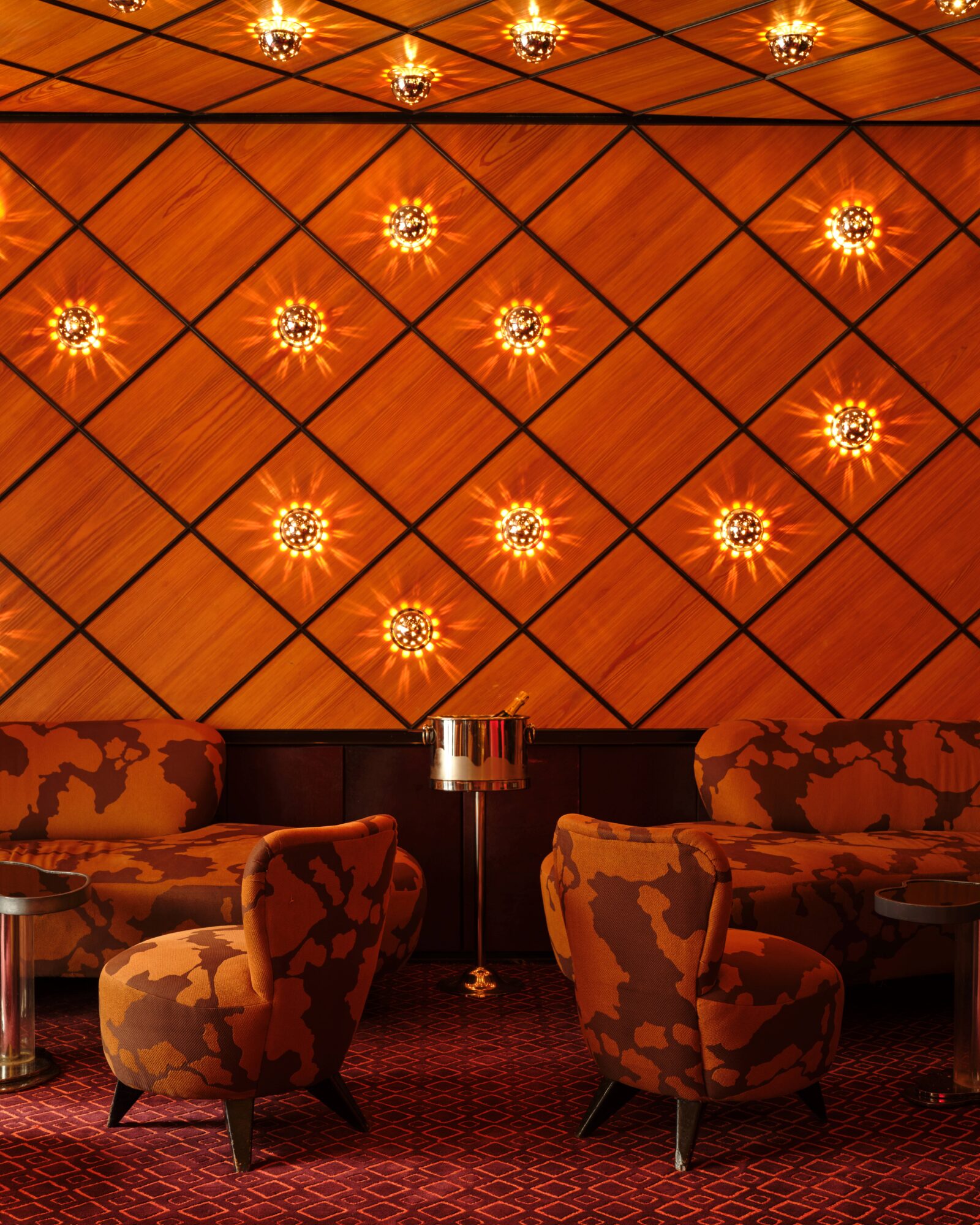 A luxurious lounge with a distinctive diamond-patterned wood ceiling and walls, featuring warm lighting and comfortable seating areas.
