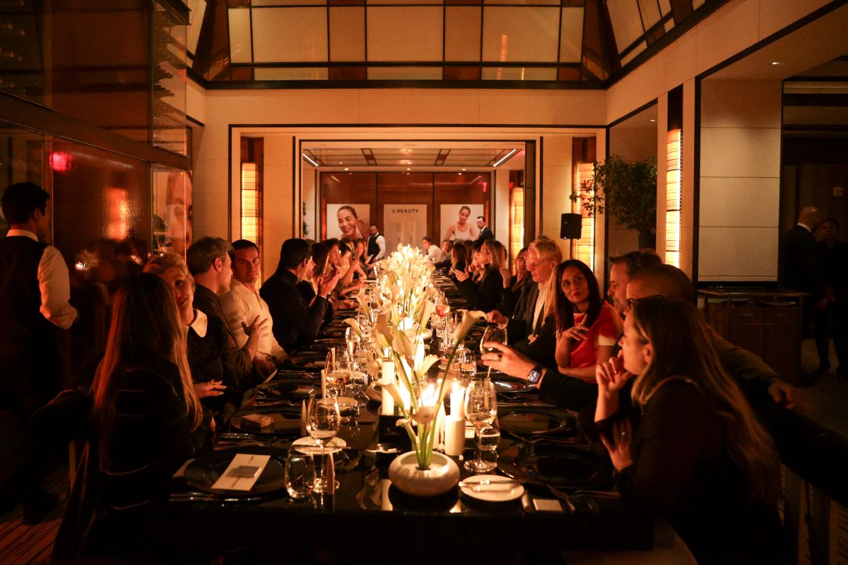 A long table set for dinner with people seated and a warm, candlelit atmosphere.